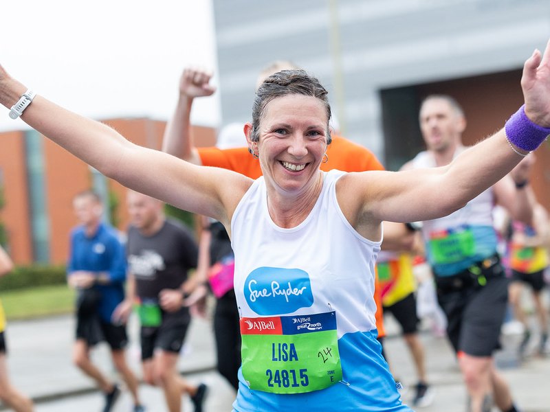 A smiling Sue Ryder runner with her hands in the air during the race