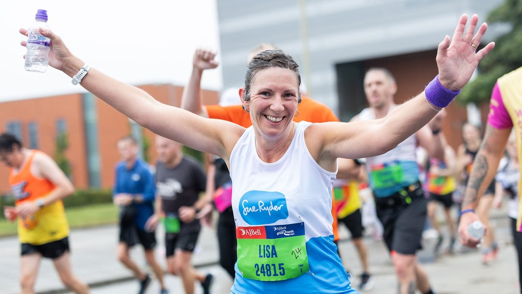 A smiling Sue Ryder runner with her hands in the air during the race