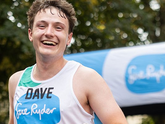 A smiling Sue Ryder runner under a Sue Ryder banner at the finish line