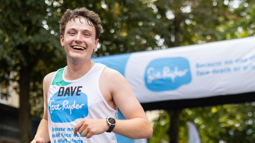 A smiling Sue Ryder runner under a Sue Ryder banner at the finish line
