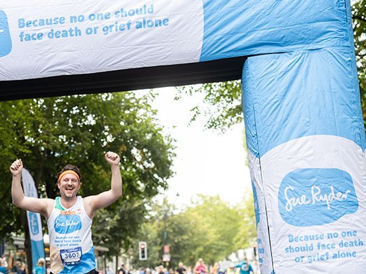 A Sue Ryder runner celebrating at the Run Cheltenham finish line, surrounded by Sue Ryder banners