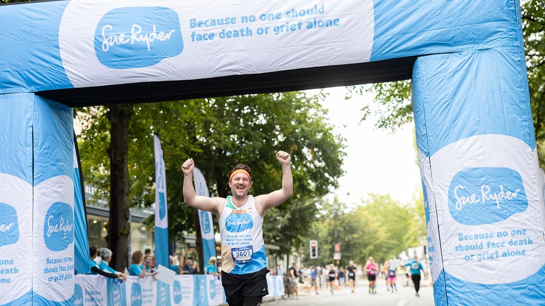 A Sue Ryder runner celebrating at the Run Cheltenham finish line, surrounded by Sue Ryder banners