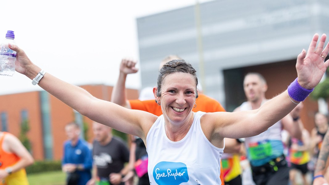 A smiling Sue Ryder runner with her hands in the air during the race