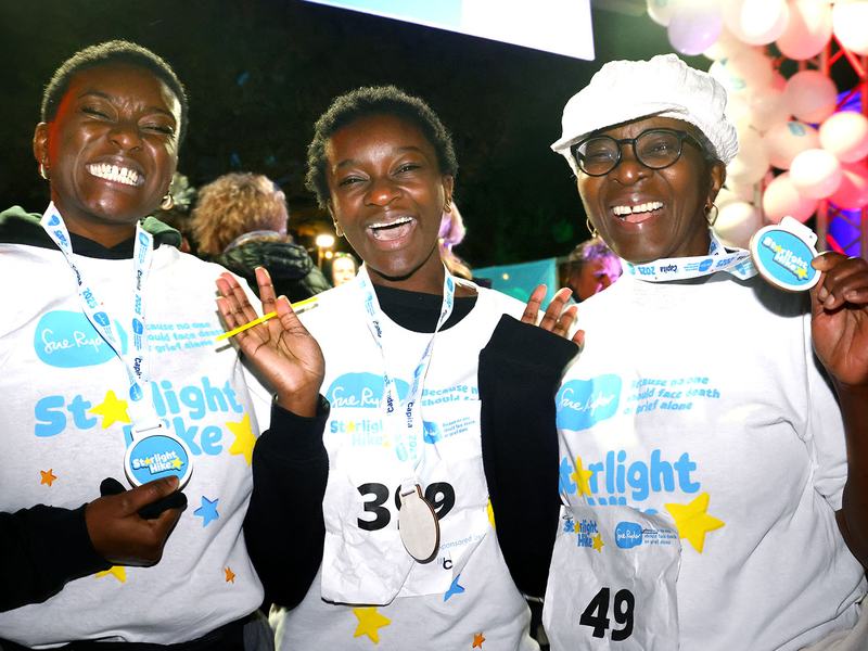 Three smiling Starlight Hike walkers at the finish line with their medals