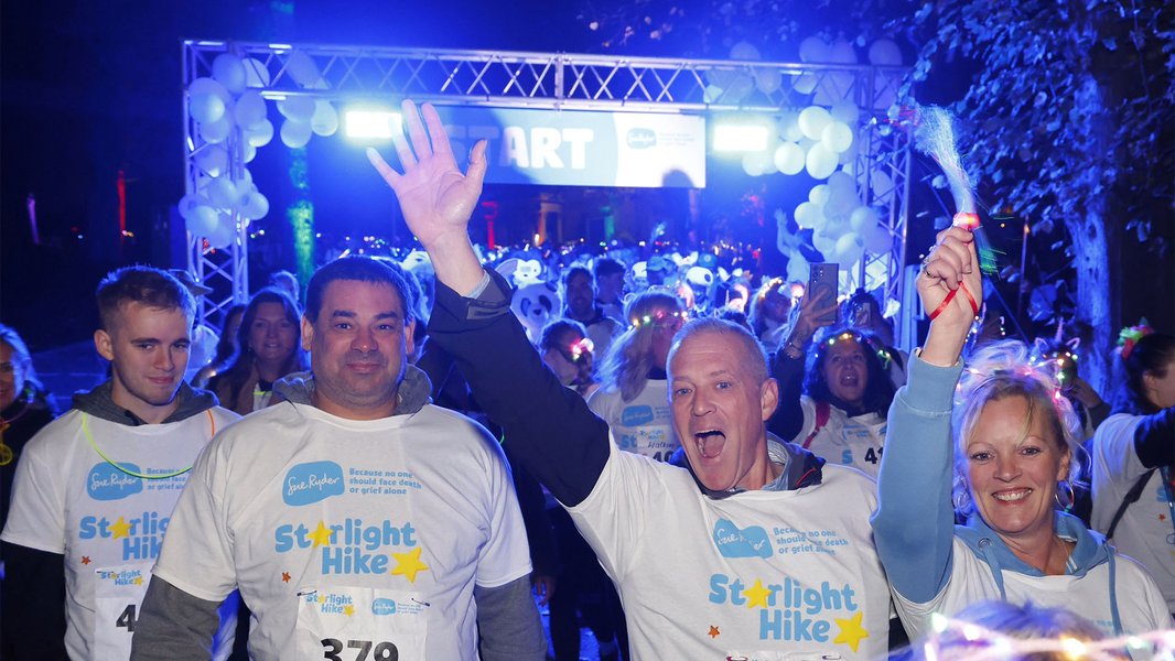 Four Starlight Hikers celebrating at the starting line, surrounded by other walkers and neon lights