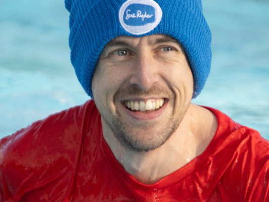 A cold water swimmer smiling, in a blue Sue Ryder winter hat