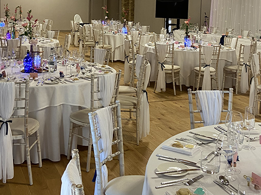 Lots of tables decorated in blue lights, with glasses, cutlery and menus on them
