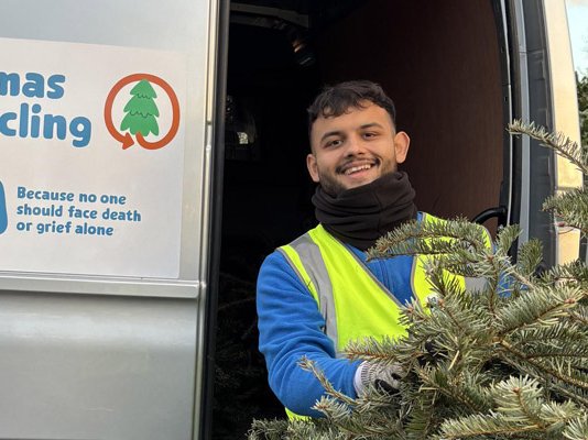 A Sue Ryder Treecycling volunteer holding a Christmas tree in front of the collection van