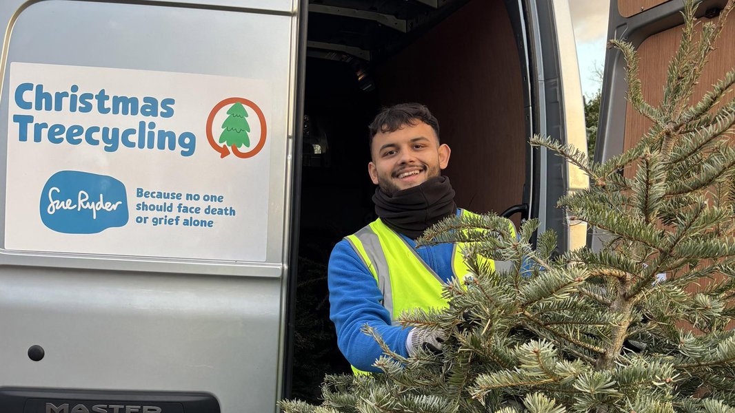 A Sue Ryder Treecycling volunteer holding a Christmas tree in front of the collection van