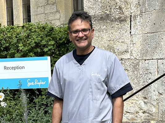 Sue Ryder volunteer Chandra, outside a hospice entrance in his green uniform