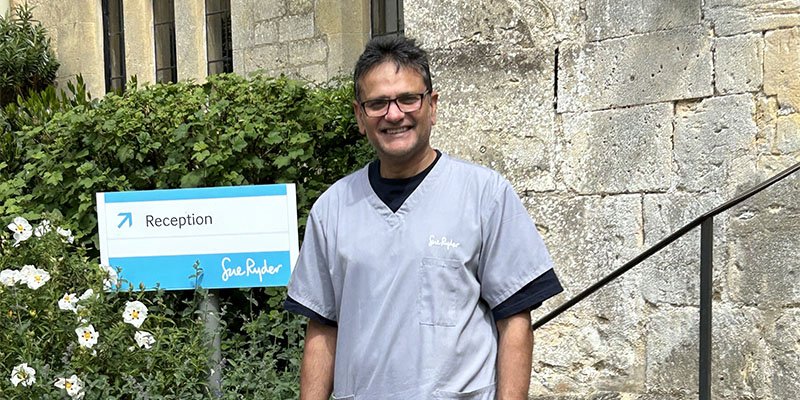 Sue Ryder volunteer Chandra, outside a hospice entrance in his green uniform