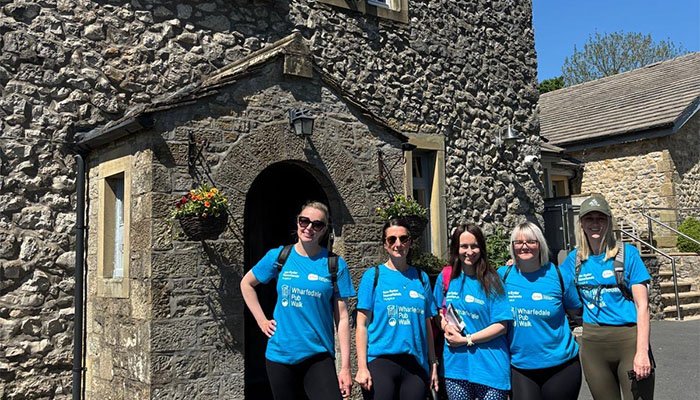 Four Sue Ryder walkers, standing together in front of a pub's stone archway entrance