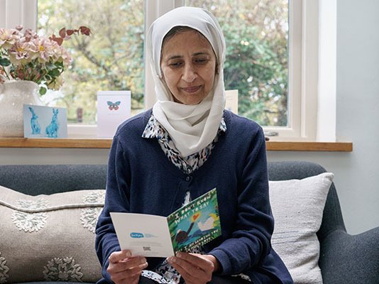 A grieving woman in a headscarf, reading a sympathy card in her living room