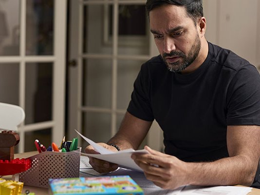 A worried-looking man sorting bills at his kitchen table after a bereavement