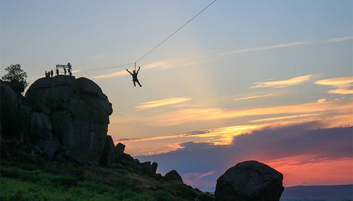 A person going down a zipwire from The Cow, with a magical sunset in the background